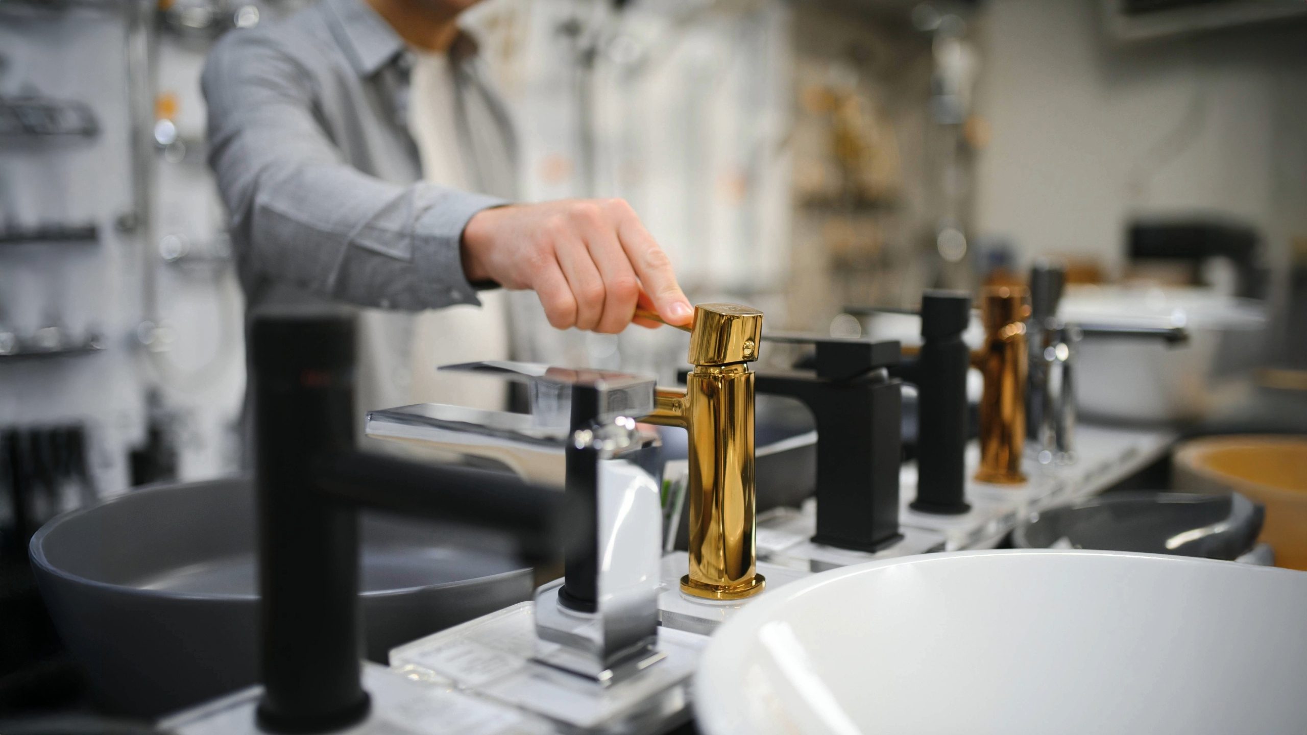 Person comparing luxury and modern sink faucet options in a showroom, showcasing finish levels and fixture choices that impact bathroom remodel cost.