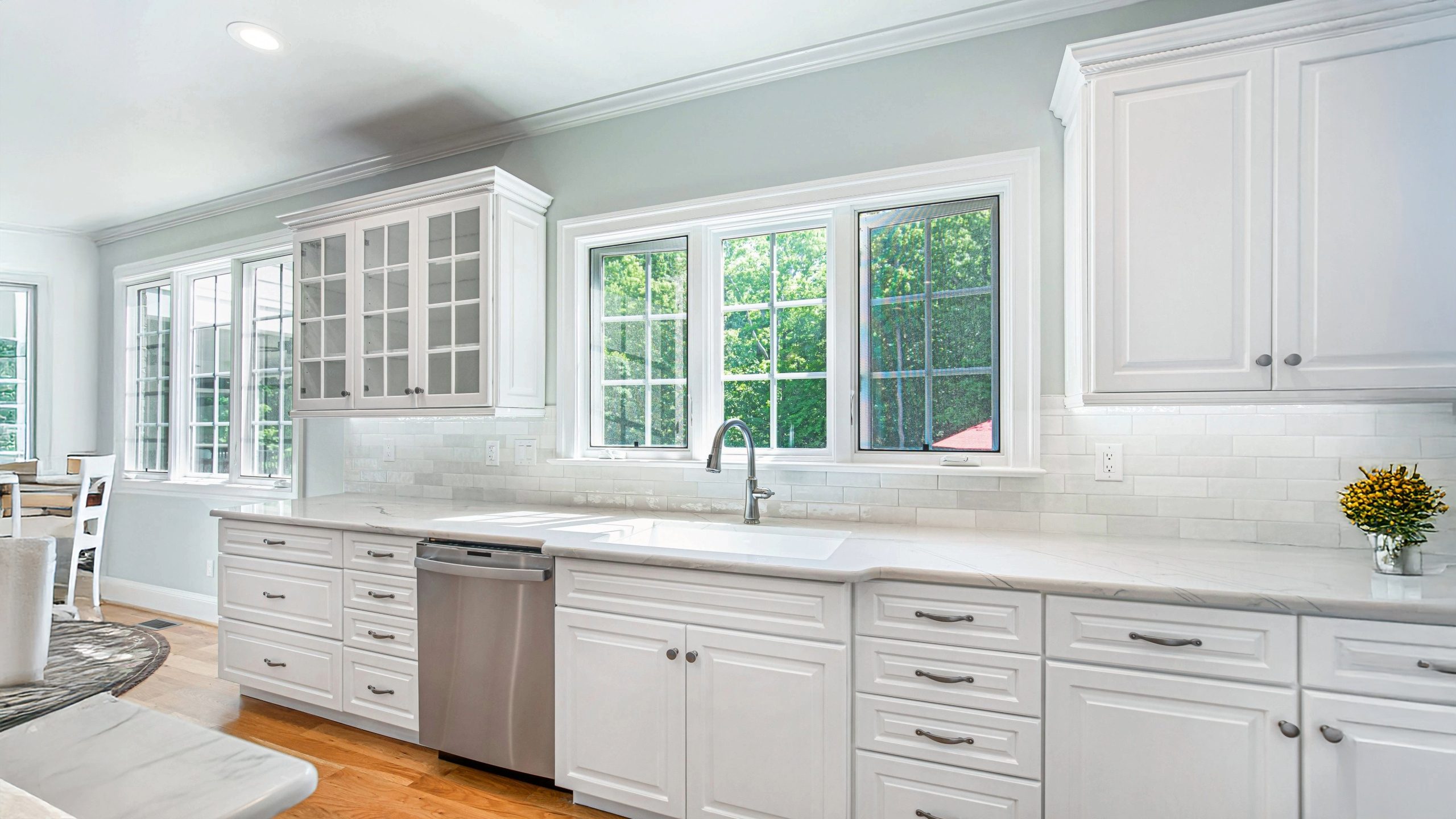 Bright and modern kitchen with white recessed-panel cabinets, quartz countertops, subway tile backsplash, and an undermount farmhouse sink beneath large windows allowing natural light to fill the space.