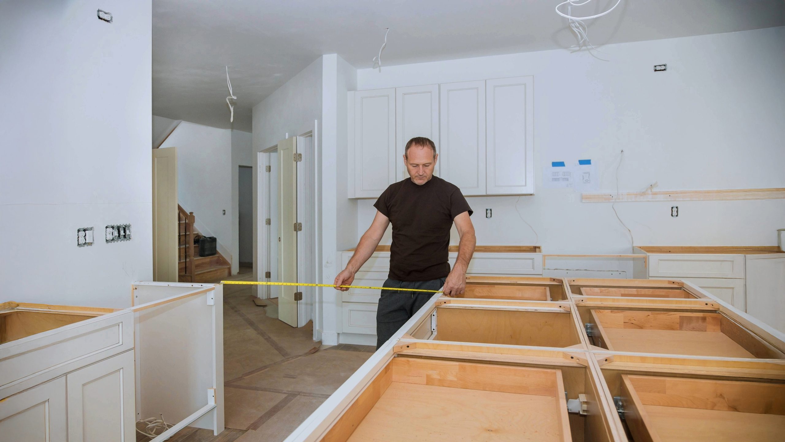 Contractor measuring kitchen island frame during a kitchen renovation near me, with white cabinets partially installed in a residential home.