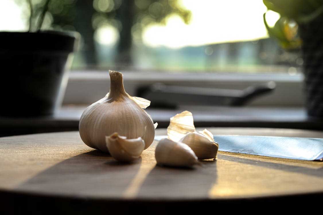 Garlic on wooden table beside a chef knife.
