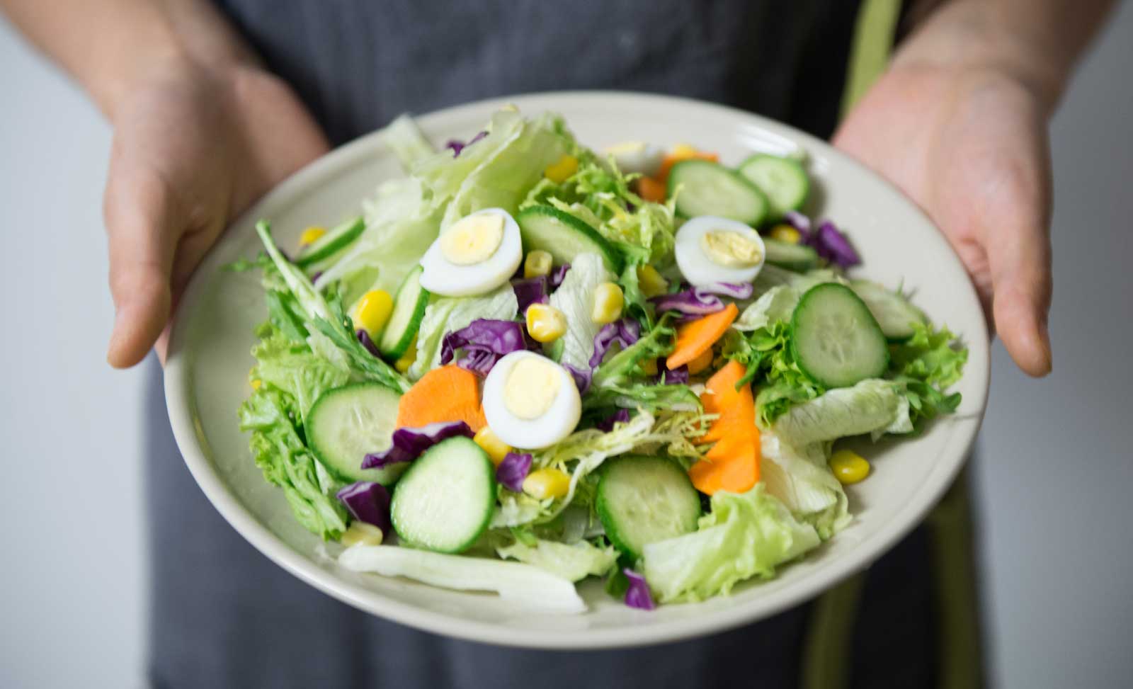 Person presenting a plate of salad, vibrant green and orange colors.