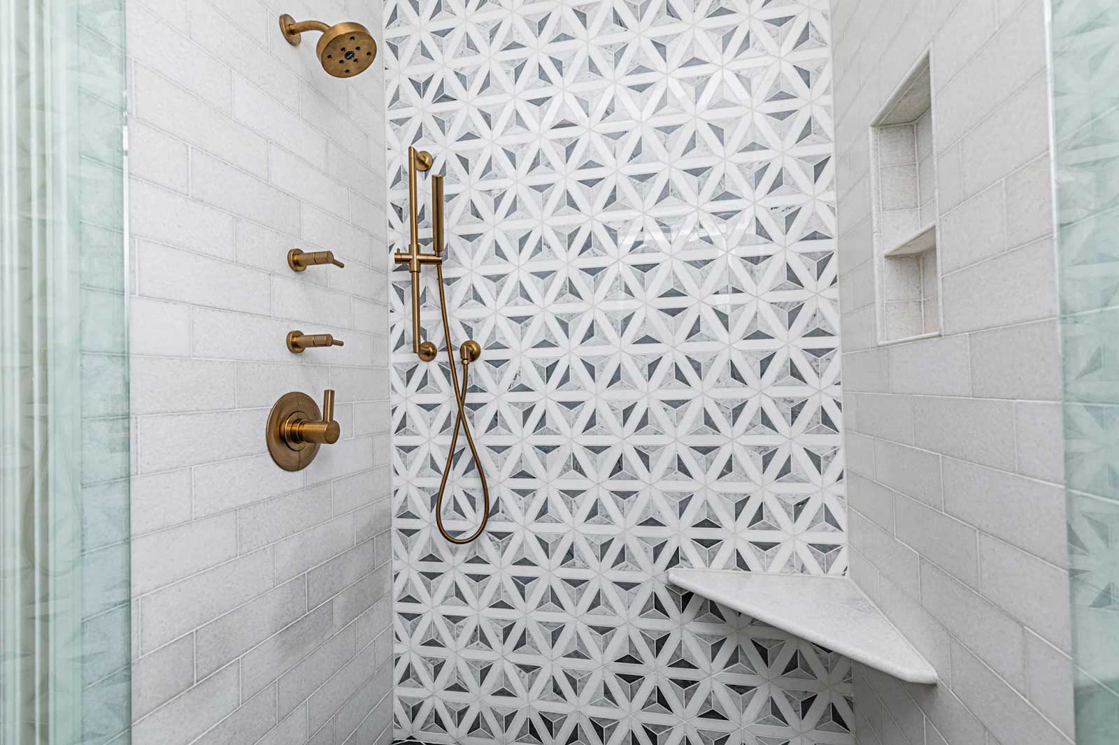 Remodeled shower featuring coordinating copper fixtures, niche, shelf, and a feature wall of patterned tiles