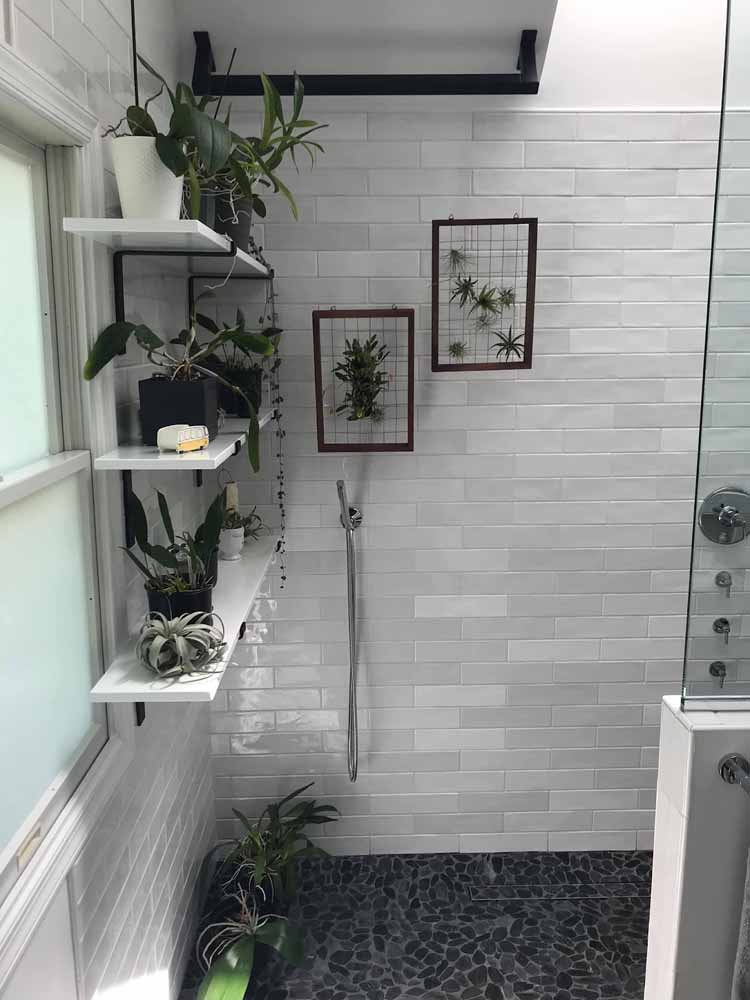 Walk in shower with shelving for plants, river rock tile floor, subway tile walls, and glass partition