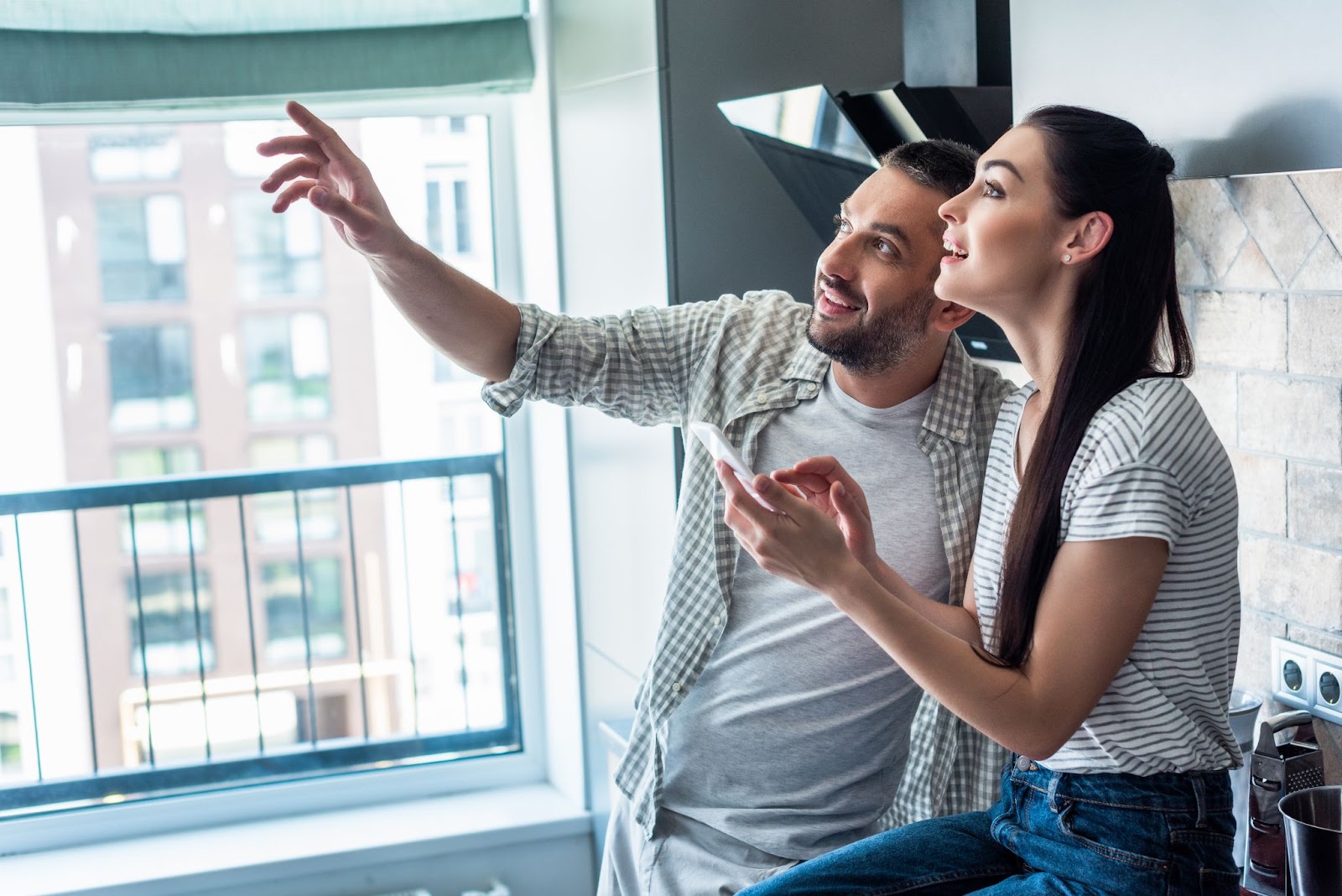 side view of smiling couple with smartphone looking away together in kitchen, smart home concept