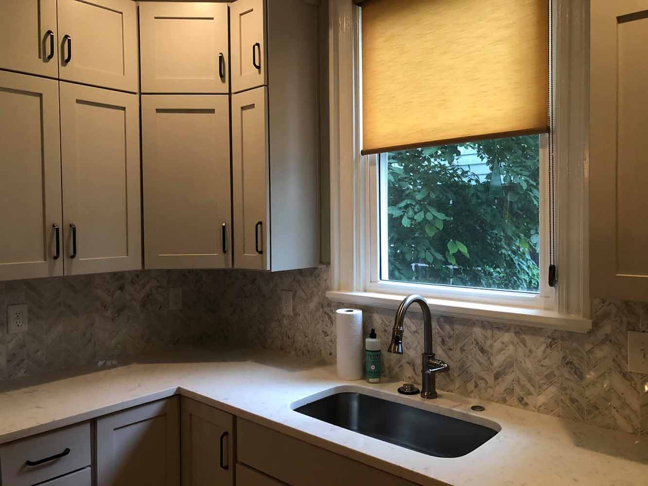 : Corner of BK Martin kitchen featuring smaller cabinets above standard kitchen cabinets to maximize storage space, next to a window and sink.